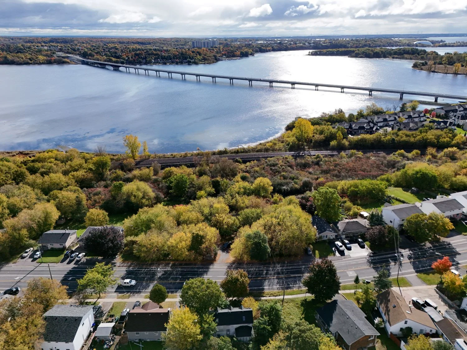 Aerial view of the Cataraqui Commons area in Kingston, with waterfront, a bridge, a railway corridor, trees and neighbouring homes.