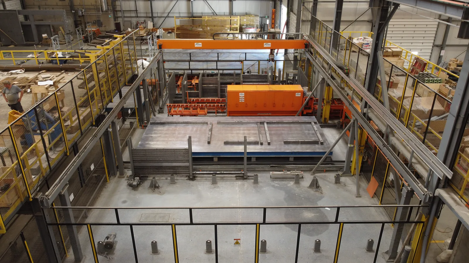 Elevated view of a precast production line with an orange gantry machine and surrounding safety platforms.