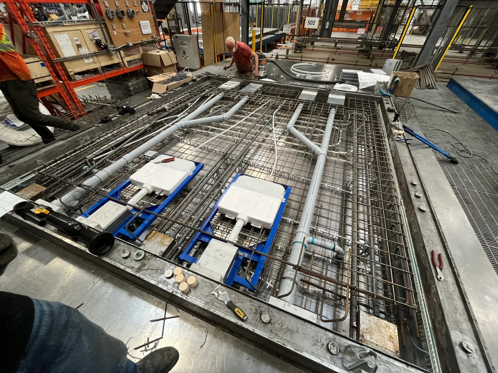 Factory production form containing reinforcement mesh, embedded tubing, blue conduit and white boxes.