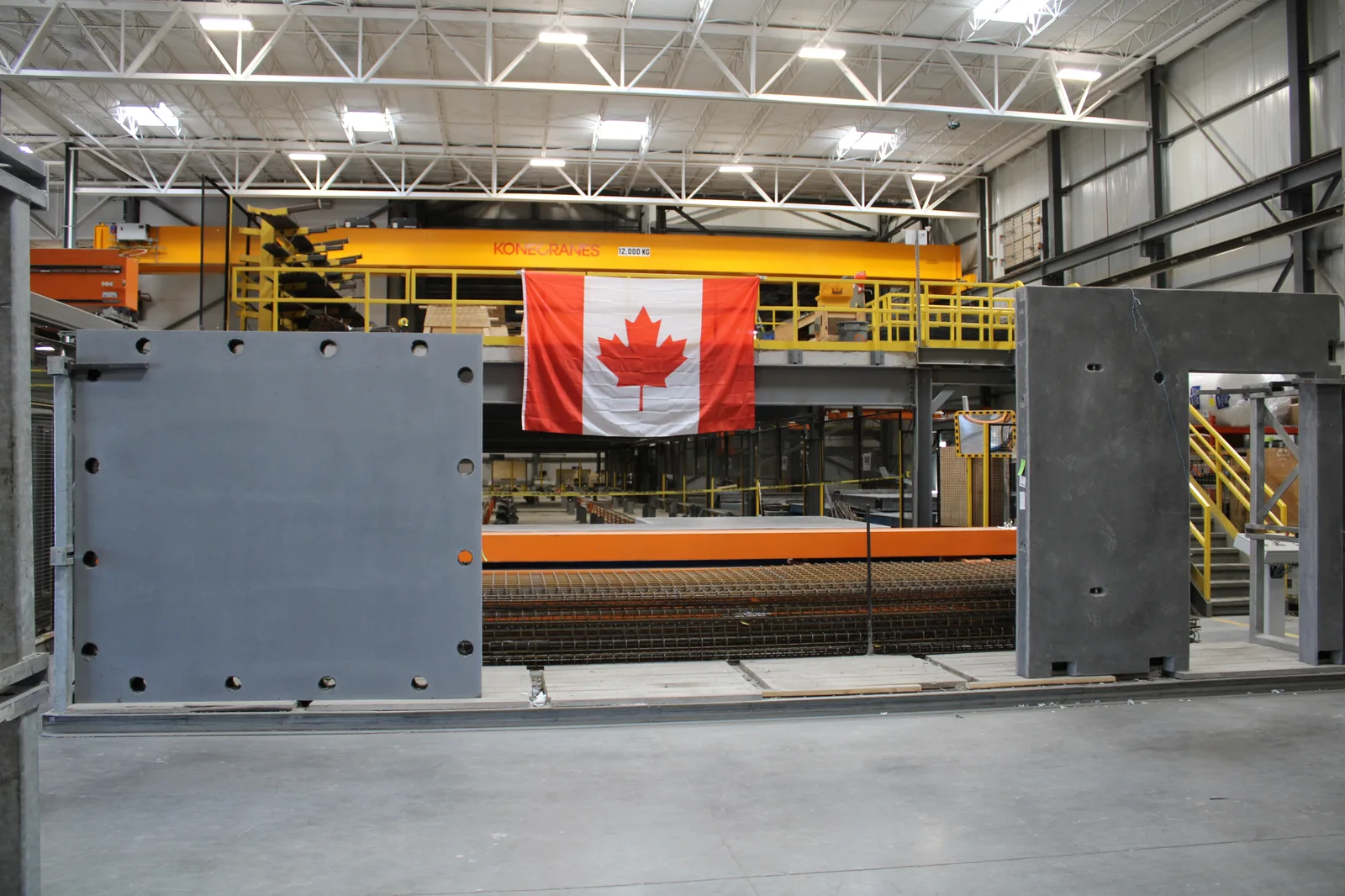 Precast wall-panel production area with yellow equipment and a Canadian flag.